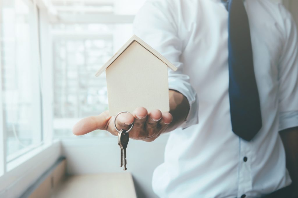 Venda ou permuta: homem com casa de madeira na palma da mão e chave pendurada no dedo